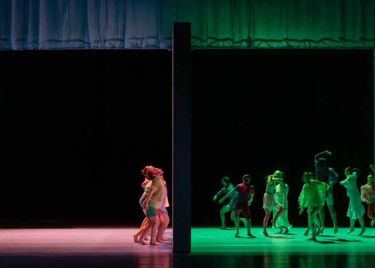 Dansare dansar på var sin sida en stor vägg som delar scenen. TIll höger om väggen dansar de i grönt ljus, till vänster i rött ljus i Skånes Dansteaters dansföreställning Out of the Blue.