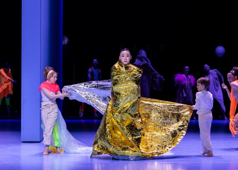 Dansaren Jing Yi Wang sveps in i ett gulddraperi av två små barn i Skånes Dansteaters dansföreställning Out of the Blue.