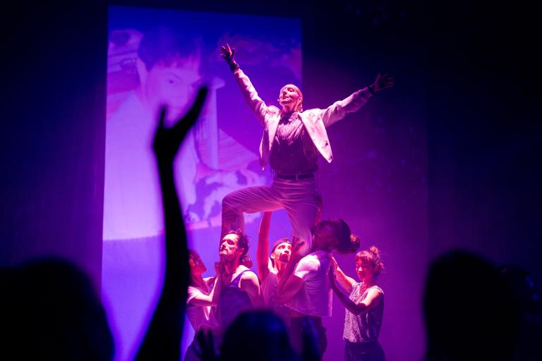 DJ:n Qarl Qunt i en triumfatorisk pose lyfts upp i luften av dansarna i Skånes Dansteaters dansföreställning Indigo Flamingo.