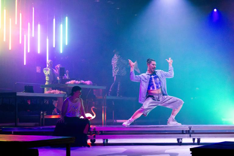Dansaren Fabrizio dansar på ett podium framför DJ-båset med regnbågsfärgade neonrör i Skånes Dansteaters dansföreställning Indigo Flamingo.