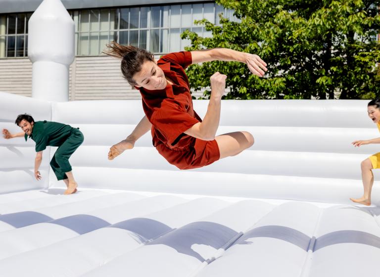 Skånes Dansteaters dansare Marion klädd i röda shorts och skjorta vänder sig i en studs i en vit hoppborg i oreografen Jernej Bizjaks dansföreställning Up-And-Down-And-Up-.