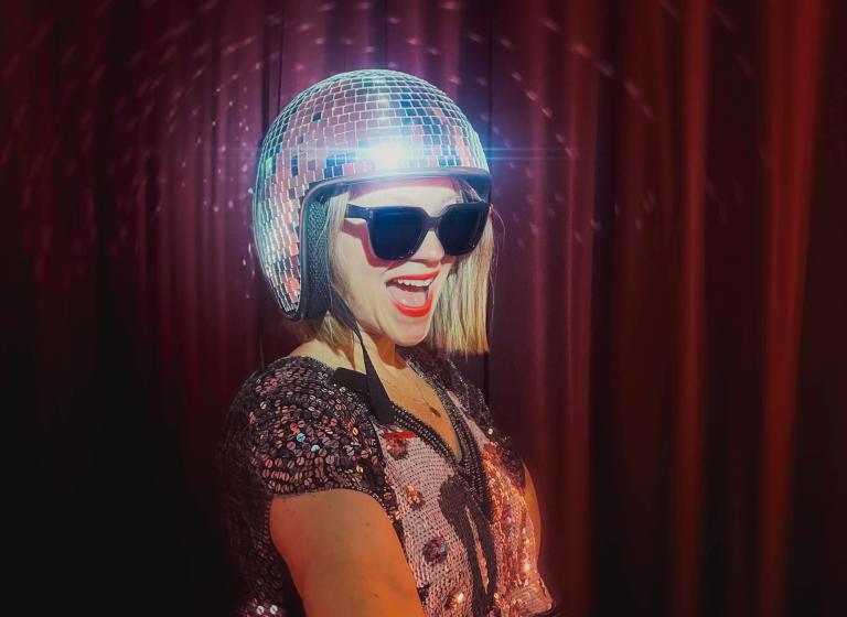 DJ Kick It klädd i discobollshjälm och solglasögon ler stort mot kameran.