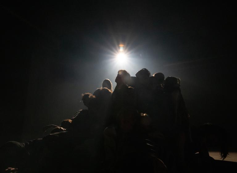 Ett tiotal dansare dansar tätt ihop som en kulle. I starkt strålkastarljus syns de i motljuset likt ett moln.