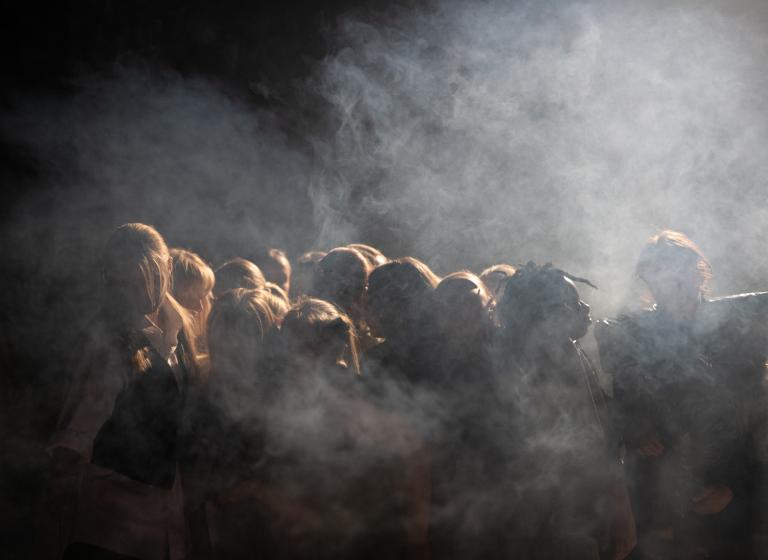 Ett tiotal dansare dansar tätt ihop i ett rökigt strålkastarljus.