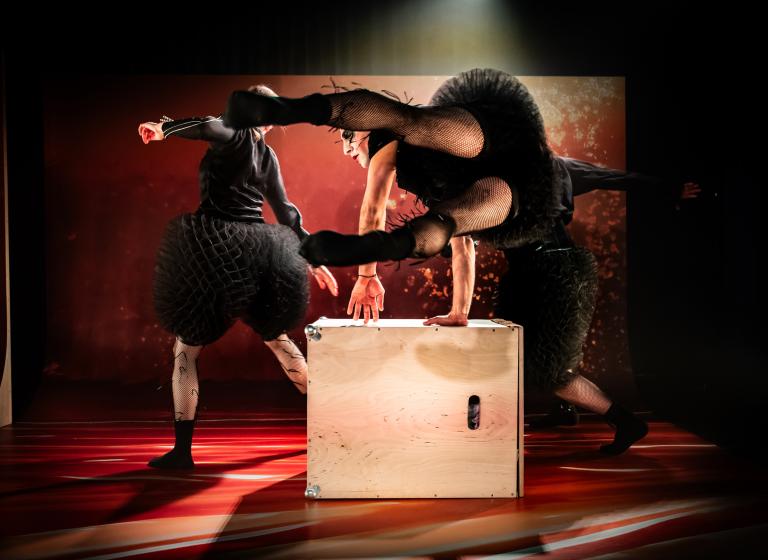 Dansare i svarta bulliga kläder dansar runt och hoppar över en låda i dansföreställningen Honey Honey.