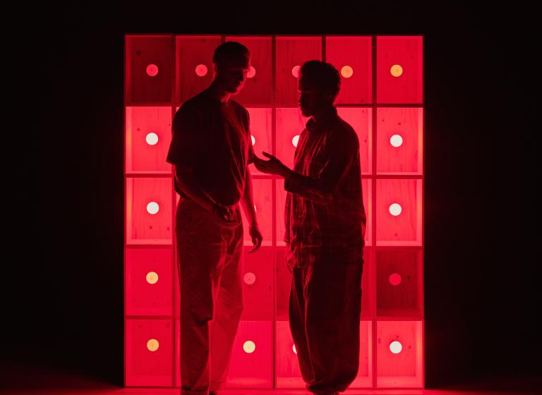 Dansarna Viktor och Yared pratar tillsammans framför en lysande röd vägg.