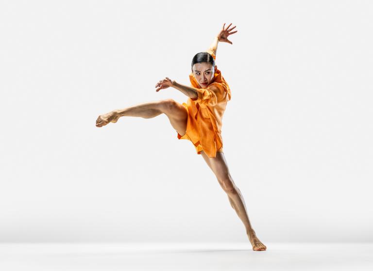 Dansaren Jing Yi Wang tar ett stort steg i sidled med armarna svängande framför och bakom sig.