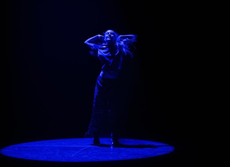 En ung dansare dansar med armarna böjda i en cirkel av blått ljus.