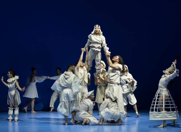 Dansare klädda i vita kläder med historiska detaljer står tätt och hissar upp dansaren Jing Yi Wang i Skånes Dansteaters dansföreställning Out of the Blue.