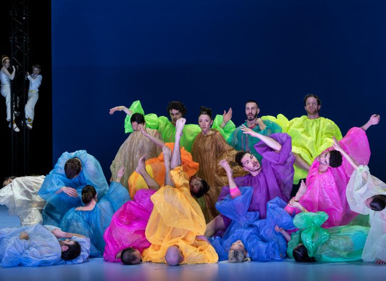 Dansare klädda i genomskinliga och färgglada luftiga overaller står i en grupp i Skånes Dansteaters dansföreställning Out of the Blue.