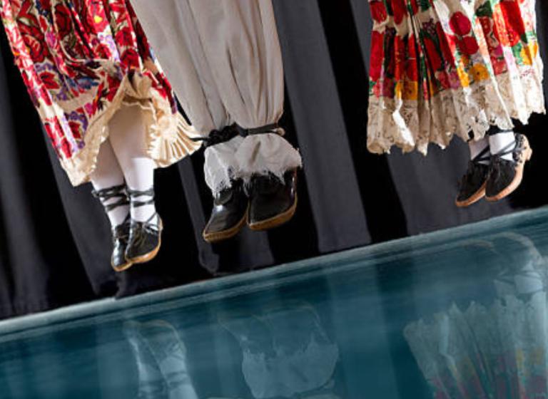 Tre par ben klädda i traditionella byxor och kjolar svävar i luften som i ett synkroniserat hopp.