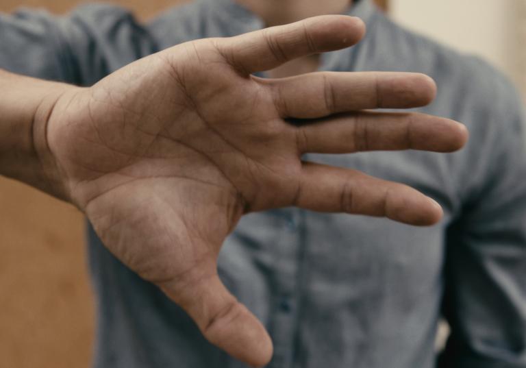 En dansare i blå skjorta håller fram sin öppna hand mot dig. 