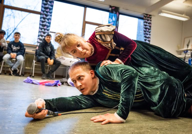Två dansare klädda i mörkröd, mörkgrön och guldiga sammet ligger på sidan ovanpå varandra i Regionteater Västs dansföreställning Sch!