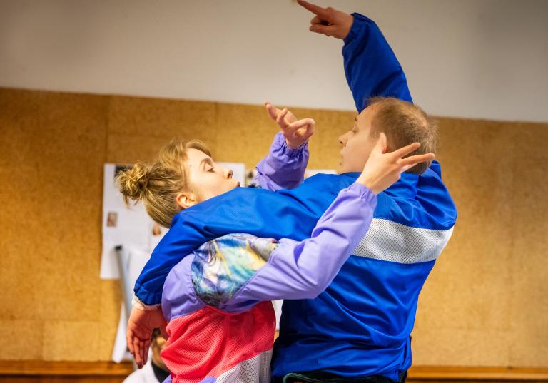 Två dansar står tätt intil och gestikulerar med sina händer. 