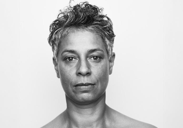 En svartvit porträttbild på dansaren och koreografen Maria Naidu med kort, lite lockigt svart-grått hår.
