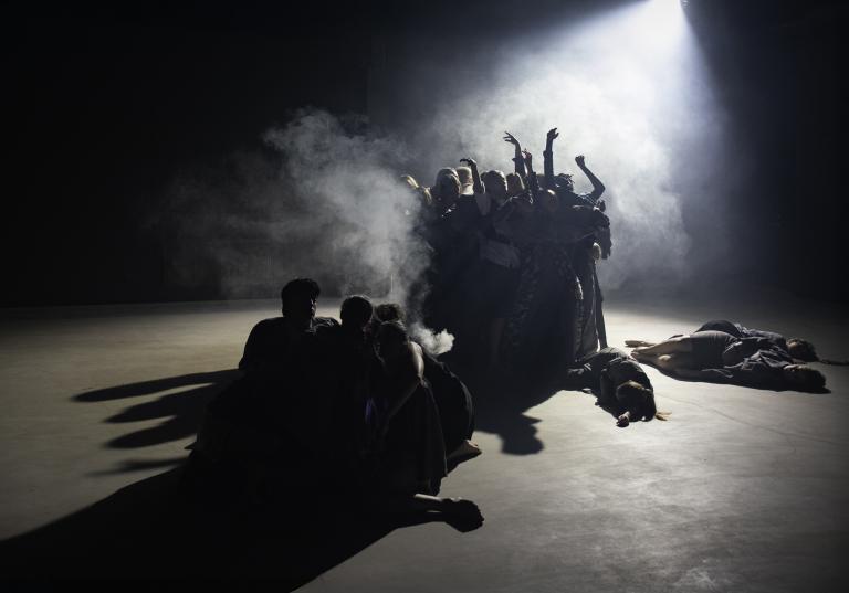 Två grupper av dansare rör sig på en scen. Ena gruppen dansar i ett rökigt strålkastarljus. Den andra gruppen rör sig i deras skugga nära golvet.