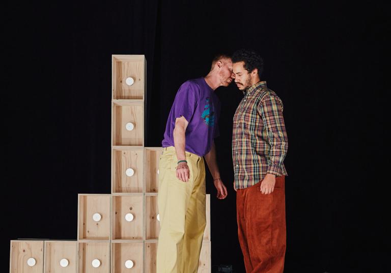 Dansarna Vitkor och Yared står tätt ihop vid staplade omålade träboxar.