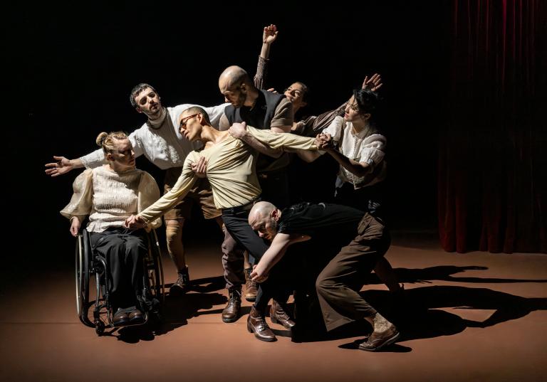 Sju dansare koreograferade som en Pietá där sex dansare dramatiskt håller en dansares kropp mellan sig.