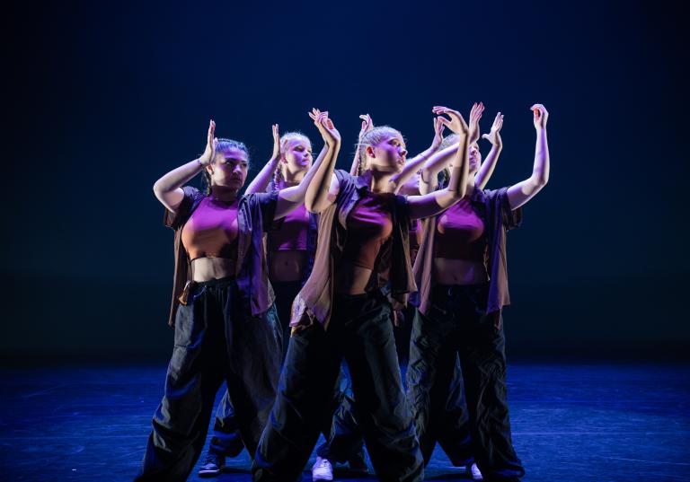 Unga dansare står tätt ihop med armarna i vinkel framför sig.