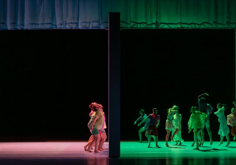 Dansare dansar på var sin sida en stor vägg som delar scenen. TIll höger om väggen dansar de i grönt ljus, till vänster i rött ljus i Skånes Dansteaters dansföreställning Out of the Blue.