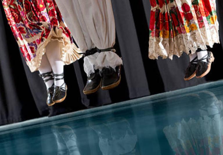 Tre par ben klädda i traditionella byxor och kjolar svävar i luften som i ett synkroniserat hopp.