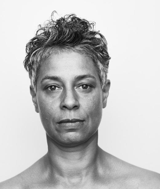 En svartvit porträttbild på dansaren och koreografen Maria Naidu med kort, lite lockigt svart-grått hår.