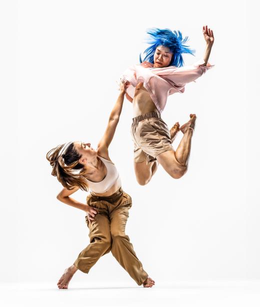 Dansaren Hanna hukar och sträcker sig upp mot dansaren Kat som hoppar högt upp i luften.