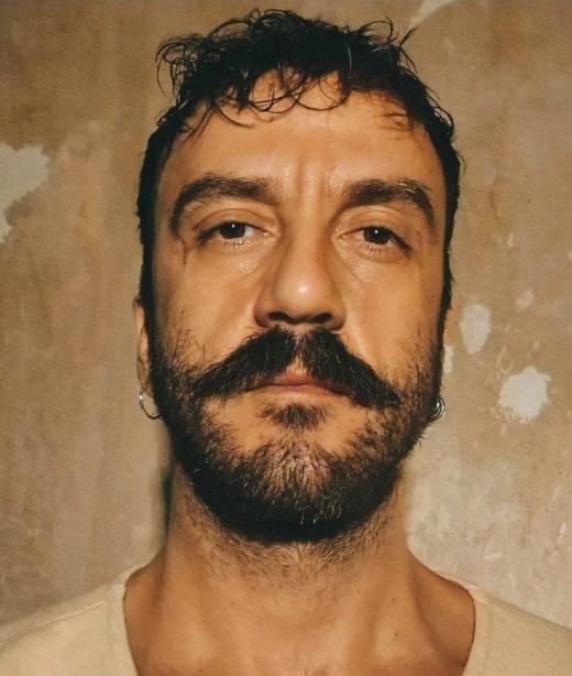 Danskonstnären Petros Mandalos med kort svart hår, skägg och mustasch klädd i en beige tröja.