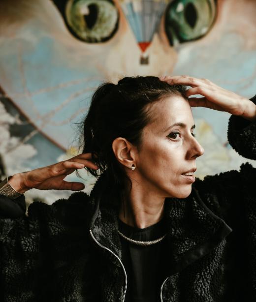 Diana Niepce står med ansiktet i profil och handerna vid ansiktet. Hon är klädd i en päls och har sitt mörka hår uppsatt.