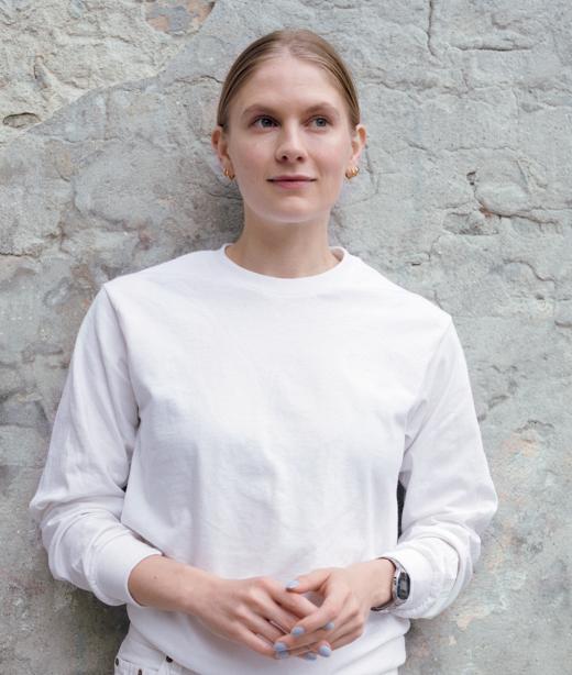 Emma Holten lutar sig mot en stenvägg klädd i vit tröja.